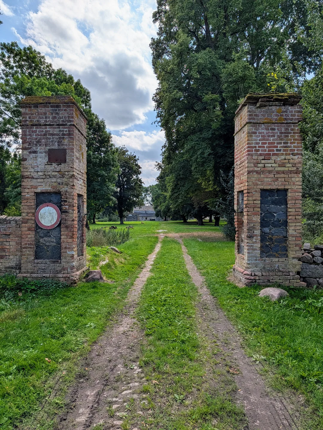 Zwei gemauerte Torpfeiler aus Ziegel mit Feldsteinfüllung, dazwischen ein Feldweg in den Park von Putzar