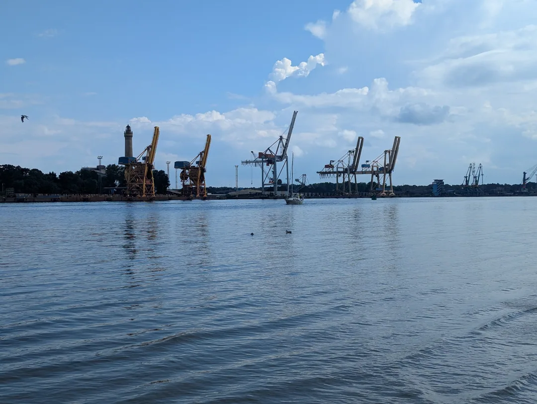 Blick über die Hafeneinfahrt von Świnoujście mit Hafenkränen und dem Leuchtturm